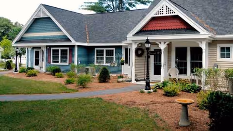 Front exterior of Havenwood Heritage Heights showing a colorful, single-story building with a landscaped lawn.