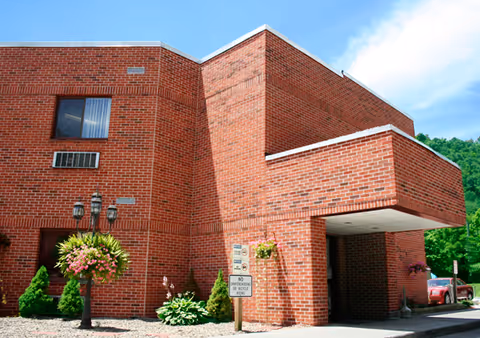 Front exterior of a red brick building with a covered entrance, hanging flower baskets, and a lamp post.