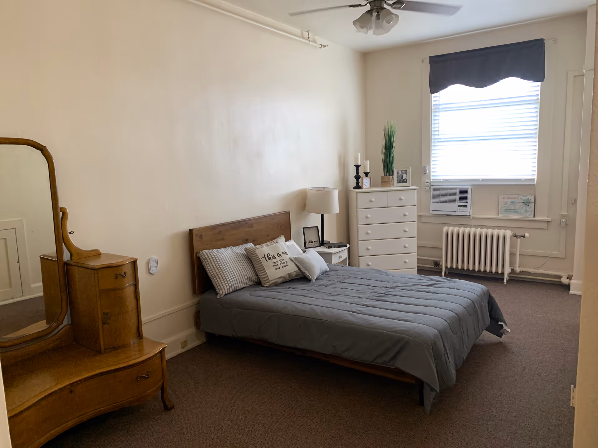 A simple bedroom features a bed, dresser, mirror, and window air conditioner.