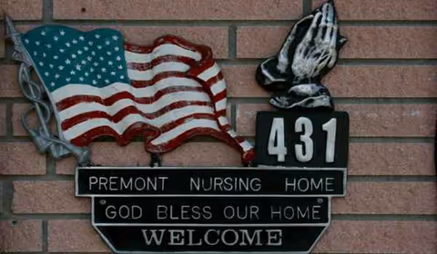 A brick wall displays a Premont Nursing Home sign with flag and Welcome message.