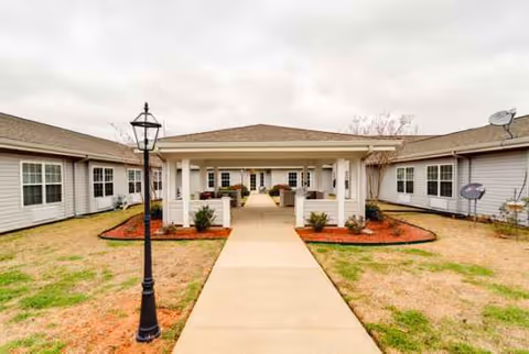 An outdoor walkway leads to a covered entrance between light colored senior living buildings.