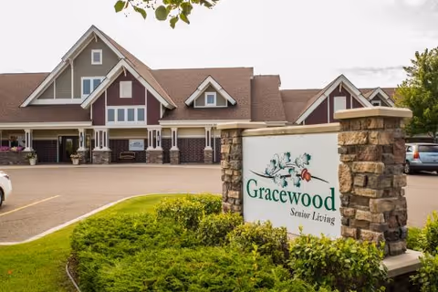 Exterior view of a senior living facility with a stone sign and parking lot.