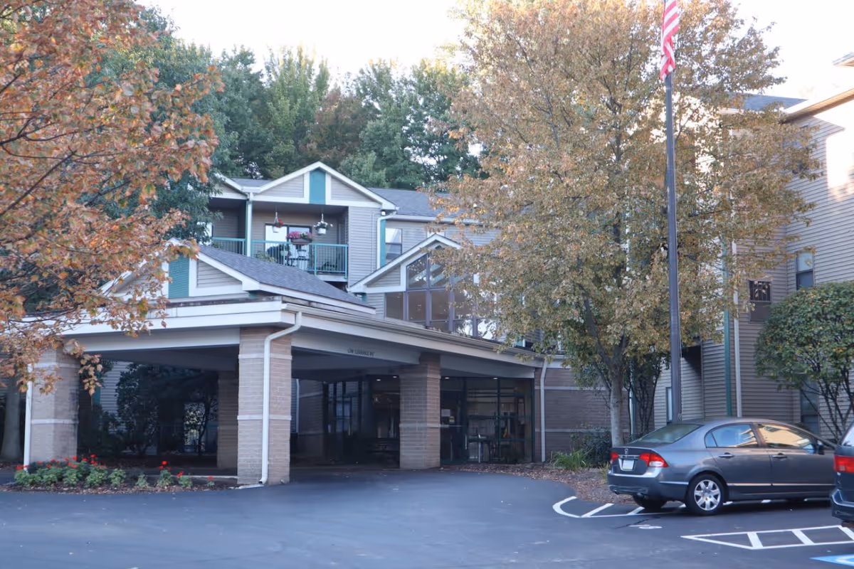 Exterior view of LECOM - Parkside at Westminster senior living facility showing the entrance with a covered drop-off area, surrounded by trees with autumn foliage and parked cars in the foreground.