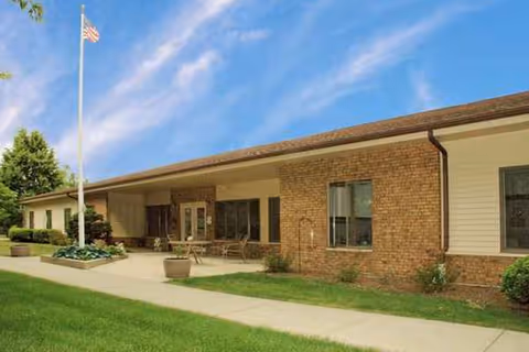 Single-story brick senior living facility exterior with flagpole and covered entrance.