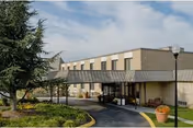 Exterior view of a two-story senior living facility building with a covered entrance driveway, landscaped greenery, and a street lamp in front.