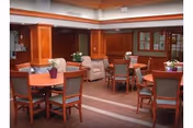 Communal dining area with round wooden tables and chairs, floral centerpieces, wood-paneled columns and cabinets.