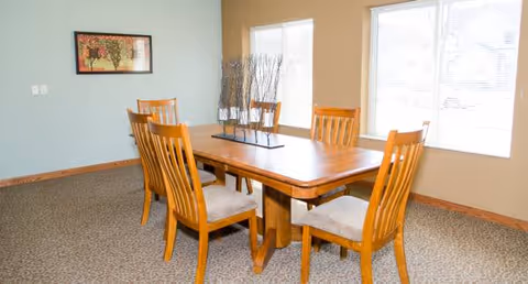 Wood dining table with six chairs in a bright, carpeted dining room.