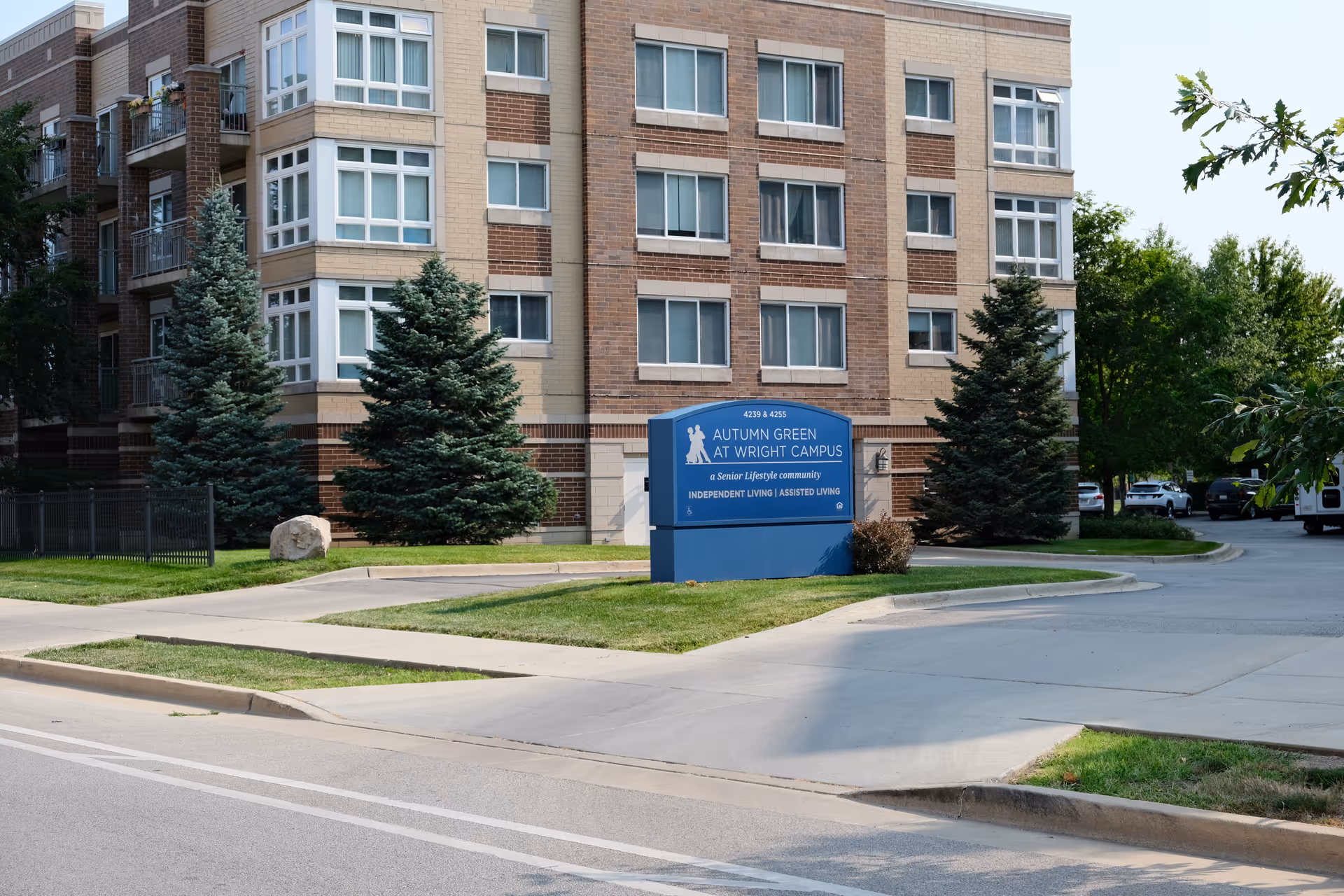Exterior front of a multi-story senior living building with a blue 'Autumn Green at Wright Campus' sign on the lawn.