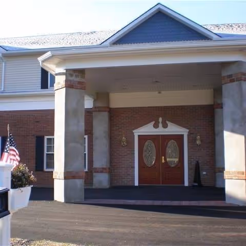 Senior living facility front entrance with brick facade, double wooden doors, columns, and an American flag.