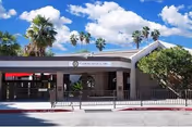 Front exterior view of Community Care & Rehabilitation Center building with a covered entrance, palm trees, and a partly cloudy sky in the background.
