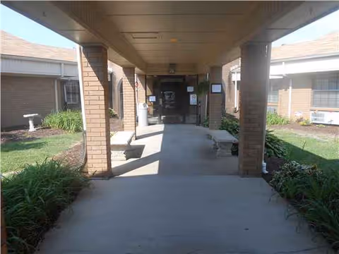 Covered exterior walkway with brick columns leading to entry doors, benches, and landscaped beds.
