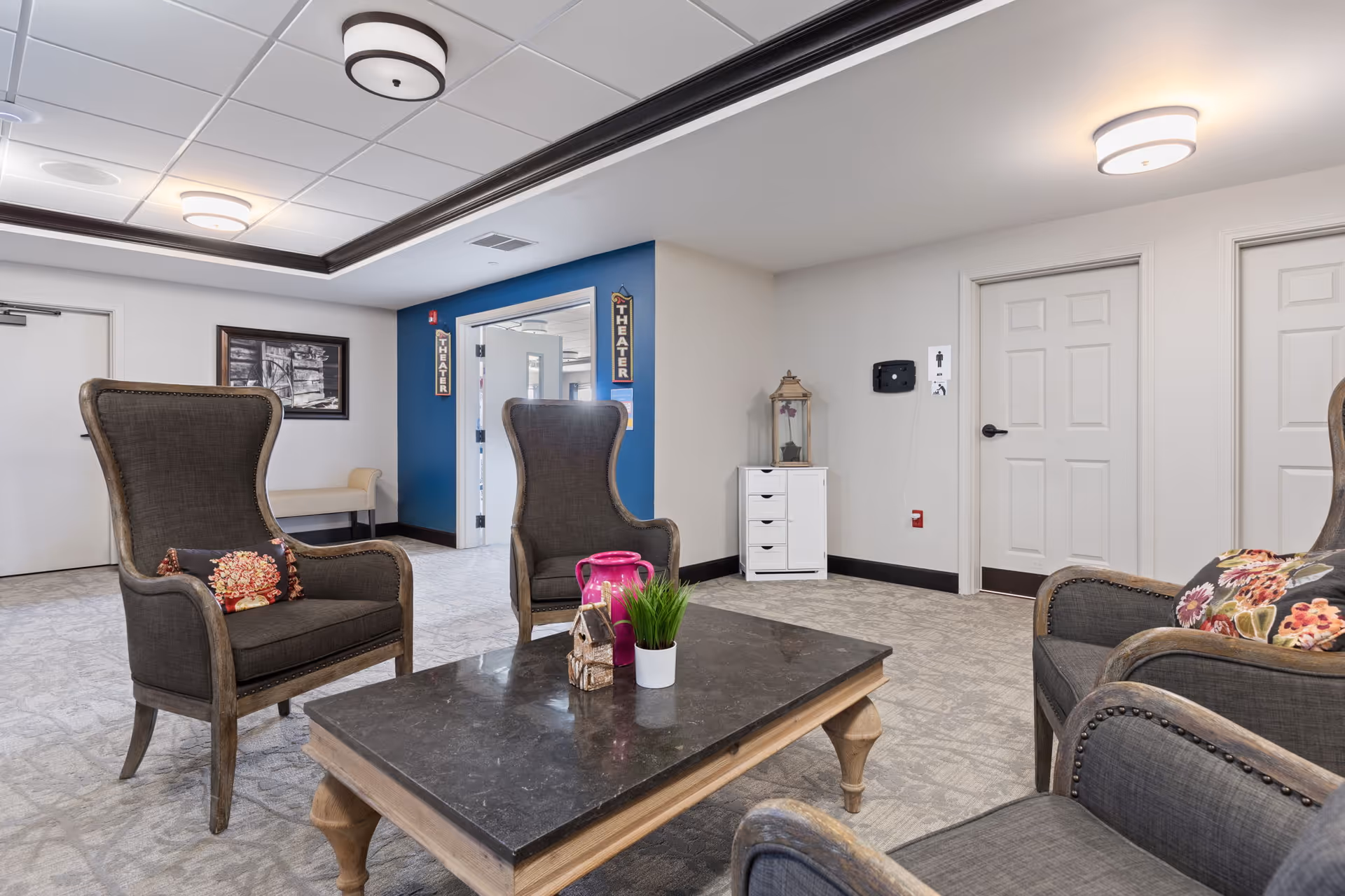 A bright communal sitting area with wingback chairs and a coffee table in a senior living facility.