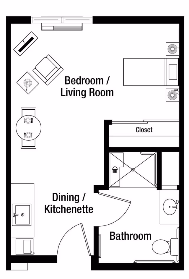 Floor plan of a senior living facility unit at Heritage Woods of Freeport showing a combined bedroom and living room area with a bed, chair, table, and closet. The unit also includes a dining/kitchenette area with a sink and microwave, and a bathroom with a shower, toilet, and sink.