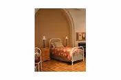 A vintage bedroom with a metal bed, floral quilt, wooden floor, and arched doorway.