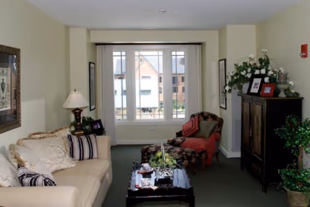 Cozy living room with a sofa, patterned armchair, coffee table and a large window with vertical blinds.