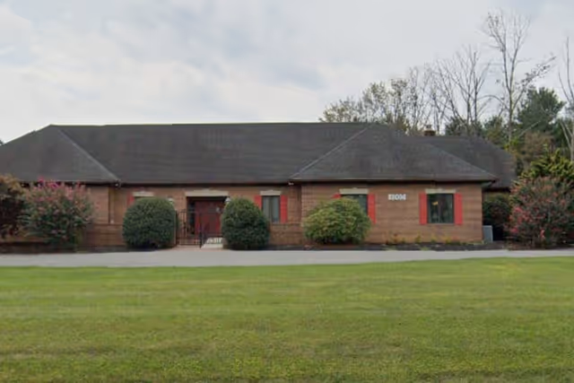 Single-story brick group home with red shutters and manicured shrubs in front yard.