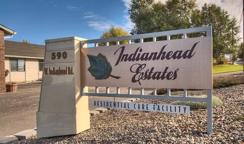 Entrance sign for Indianhead Estates Residential Care Facility reading "Indianhead Estates" with the address "590 W. Indianhead Rd." beside a gravel landscaped area.