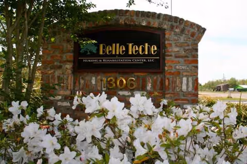 Brick entrance sign reads Belle Teche Nursing & Rehabilitation Center, with white flowers.