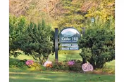 Outdoor view of a sign for Cedar Hill Health Care surrounded by green bushes and colorful flowers with trees in the background.