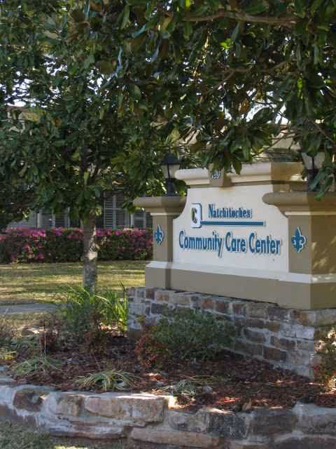Exterior view of Community Care Center sign with landscaping and trees.