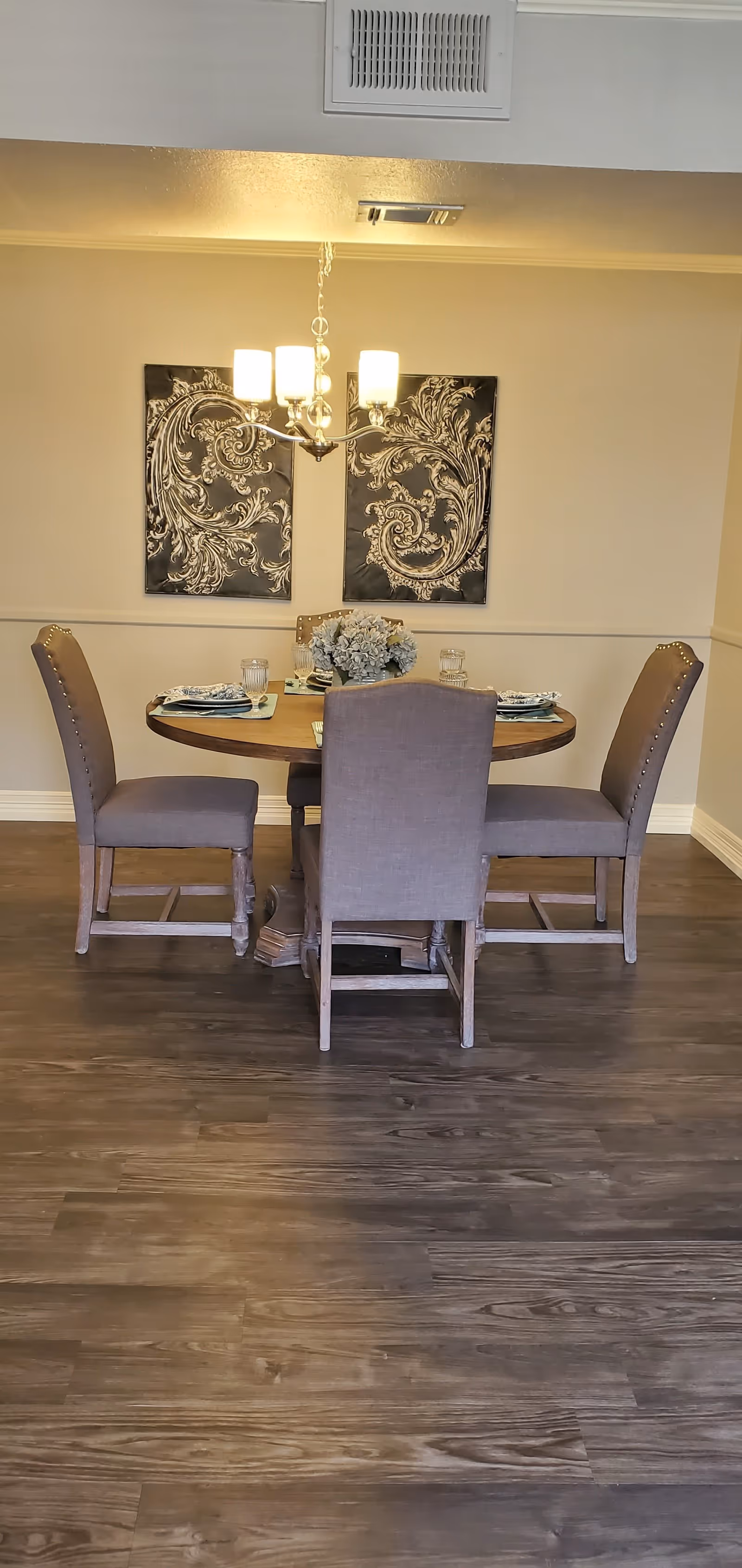 Small dining room with a round table set for four, upholstered chairs, a chandelier, decorative wall art, and wood flooring.