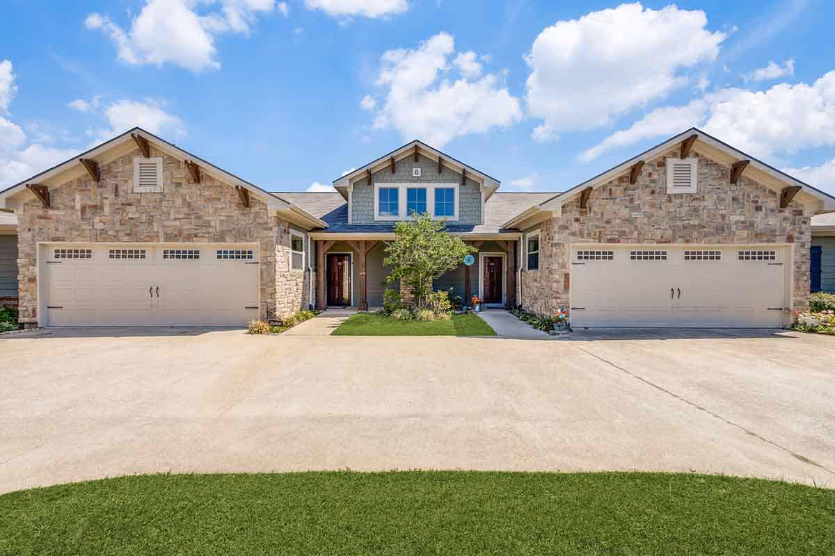 Front exterior of a single-story residential building with stone facades, two double-car garage doors flanking a central entry under a blue sky.