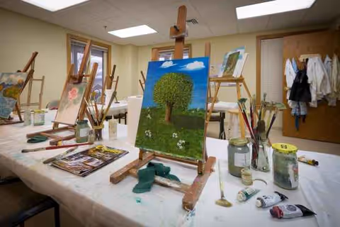 Indoor art studio at The Glebe with easels, brushes, and a tree painting on display.