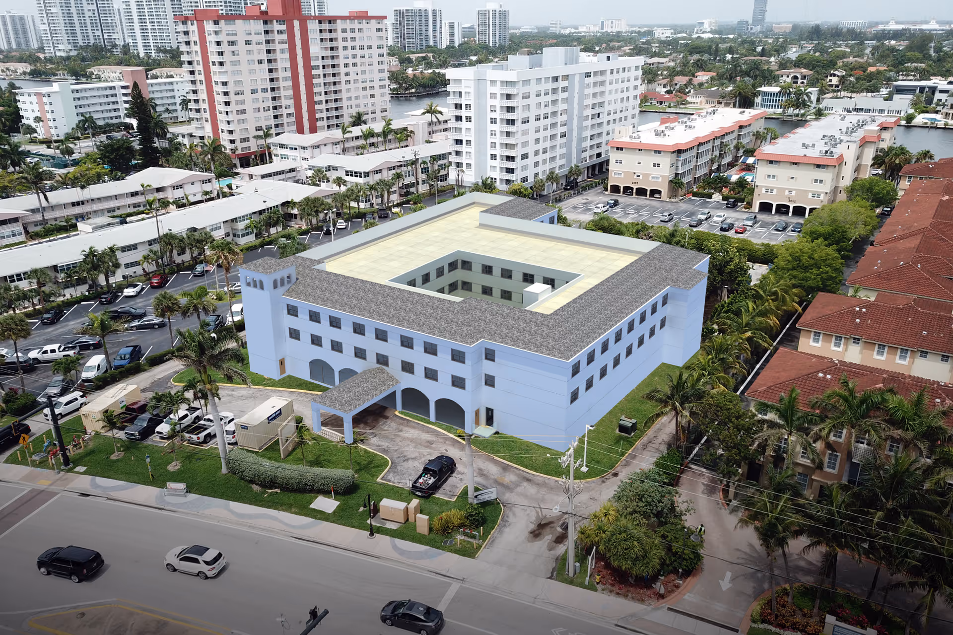 Aerial view of a multi-story senior living facility building with a central courtyard, surrounded by palm trees, parking lots, and nearby residential buildings in an urban area.