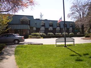Front view of a two-story building with a lawn, bench, flagpole, and parked car.