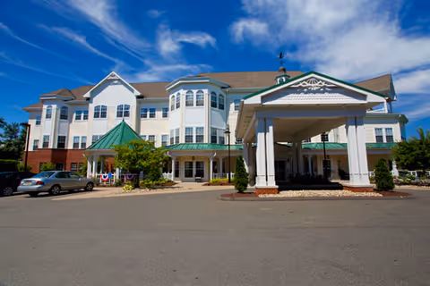 Front exterior view of a large, multi-story senior living facility named Brookdale South Windsor with a covered entrance, several windows, and a clear blue sky above.