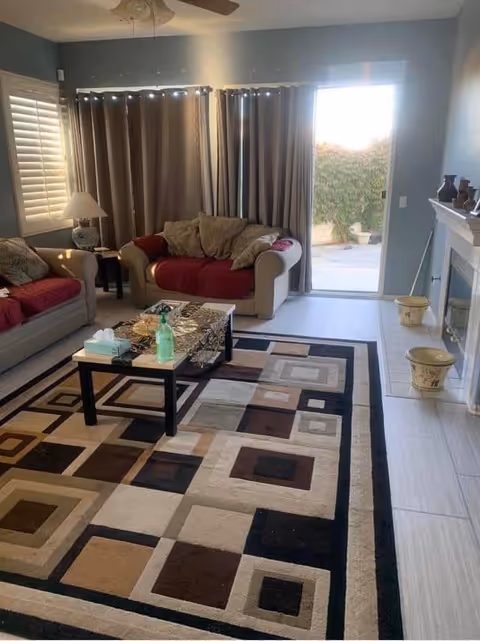 Living room with a geometric area rug, coffee table, two sofas, a fireplace, and a sliding glass door to an outdoor patio.