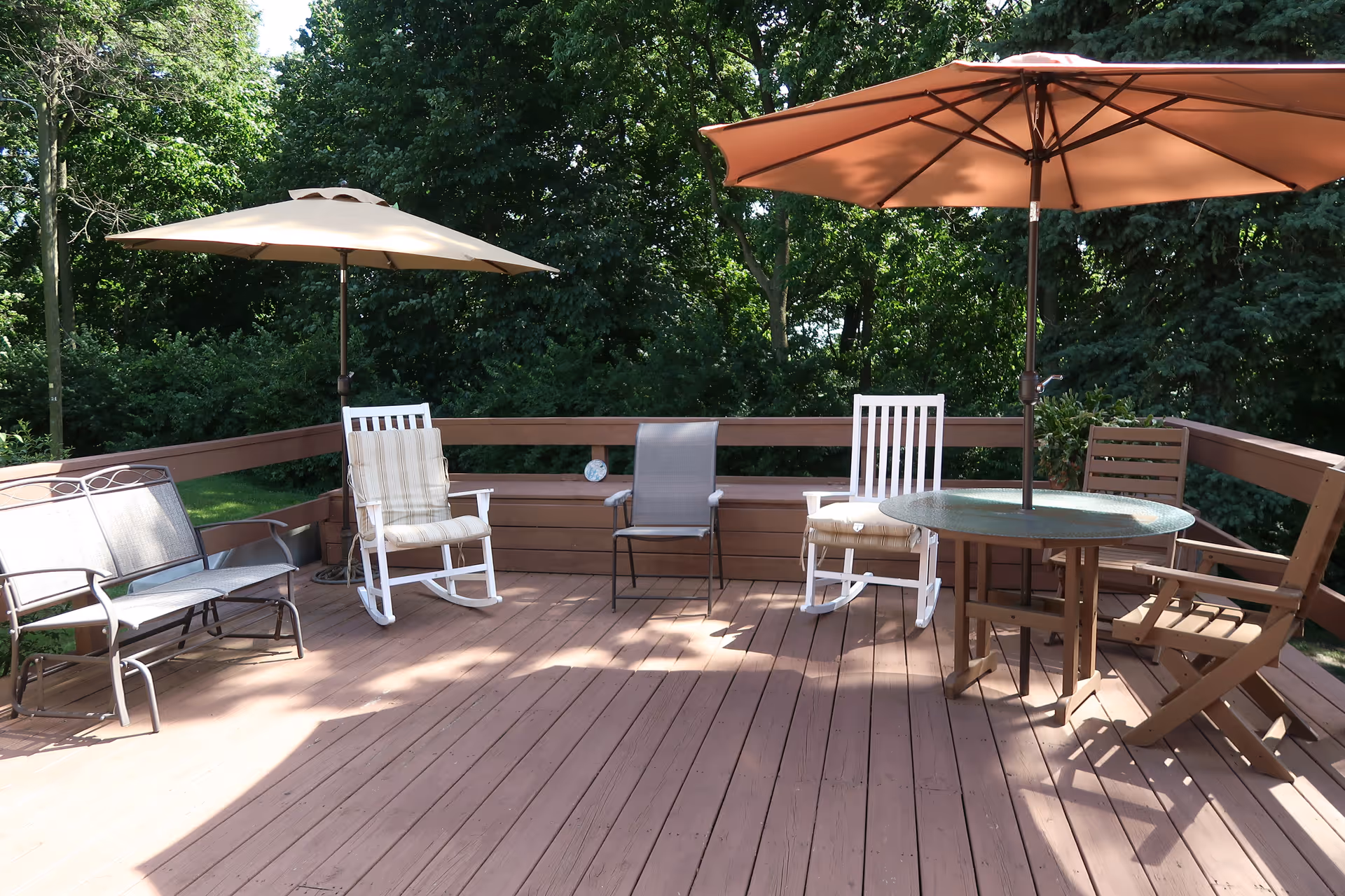 Wooden deck patio with chairs, tables, and umbrellas overlooking a tree-filled yard.