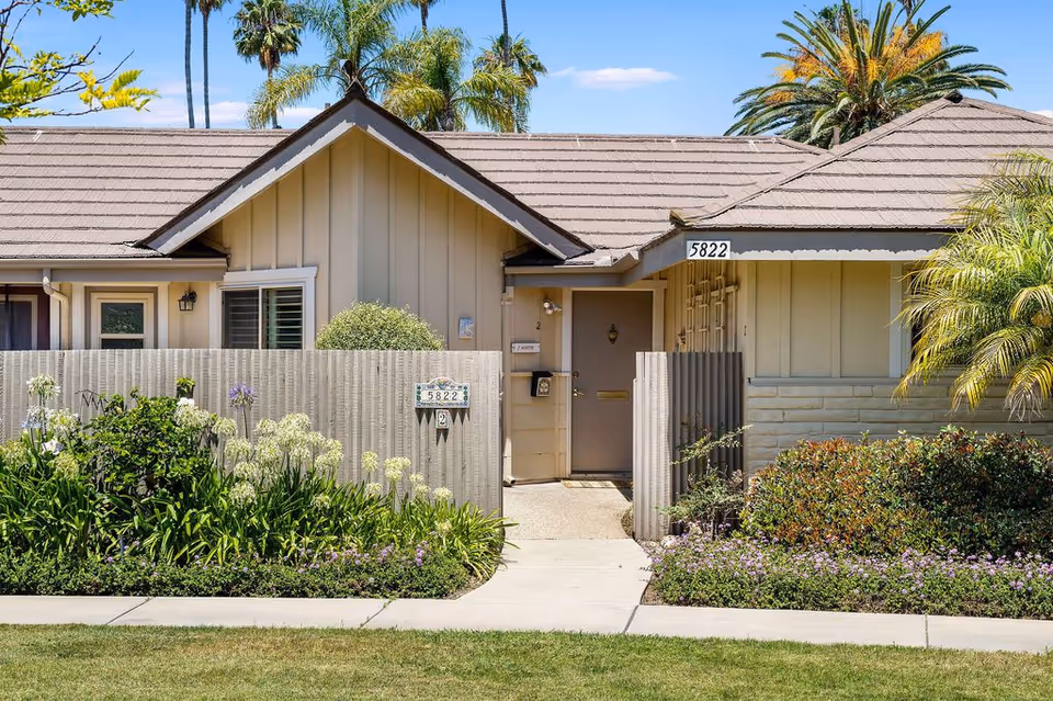 Exterior front of a single-story beige residential unit with a small fenced entry, address plaque reading 5822, and landscaped plants.