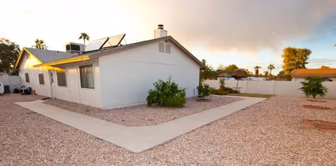 Single-story white building with solar panels, gravel yard, and concrete walkway.