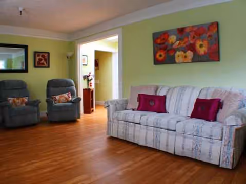 Bright green living room in Cedar Lane facility with sofa, recliners, and wall art.