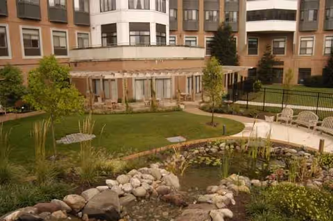 Outdoor courtyard of a senior living facility with a pond, rocks, greenery, and seating.