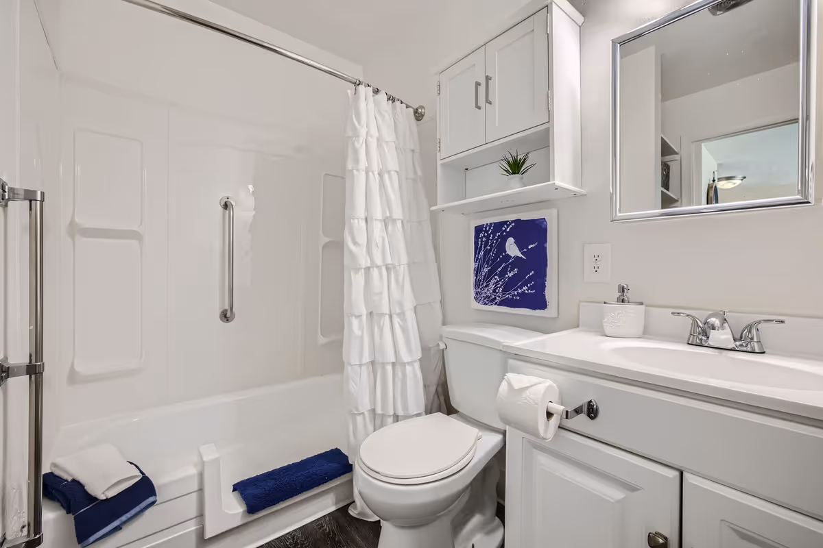Bright white bathroom with a tub/shower, toilet, vanity with mirror and wall cabinet.