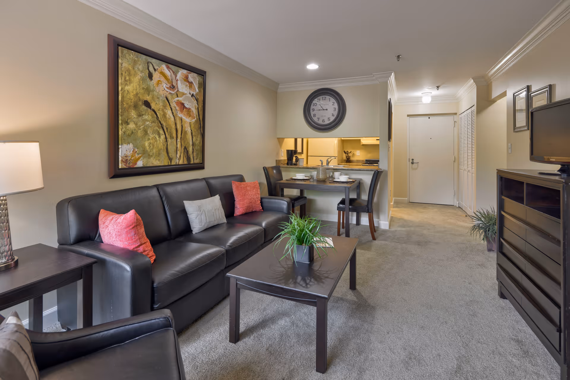 Cozy living room with a black leather sofa, coffee table, dining nook and kitchen pass-through in an apartment.