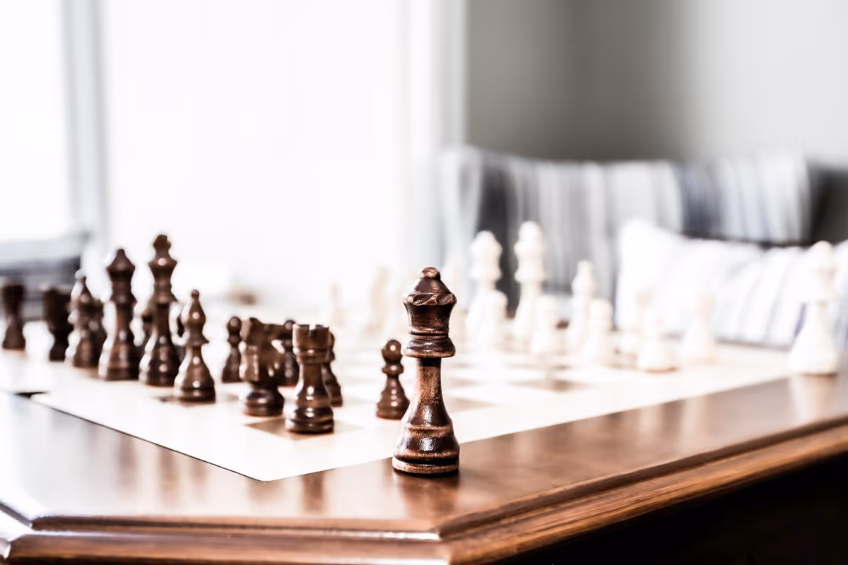 Close-up of a wooden chessboard with chess pieces set on a table in a cozy living room.