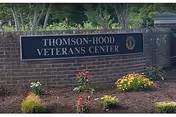 A brick sign for Thomson-Hood Veterans Center surrounded by a landscaped area with small bushes and flowers, with trees and greenery in the background.