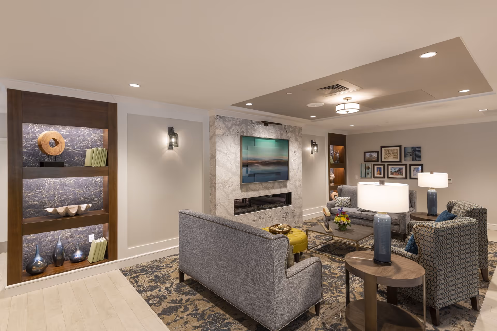 Comfortable modern living room/lounge with sofas, armchairs, a coffee table, built-in shelving, and a wall-mounted TV over a fireplace.