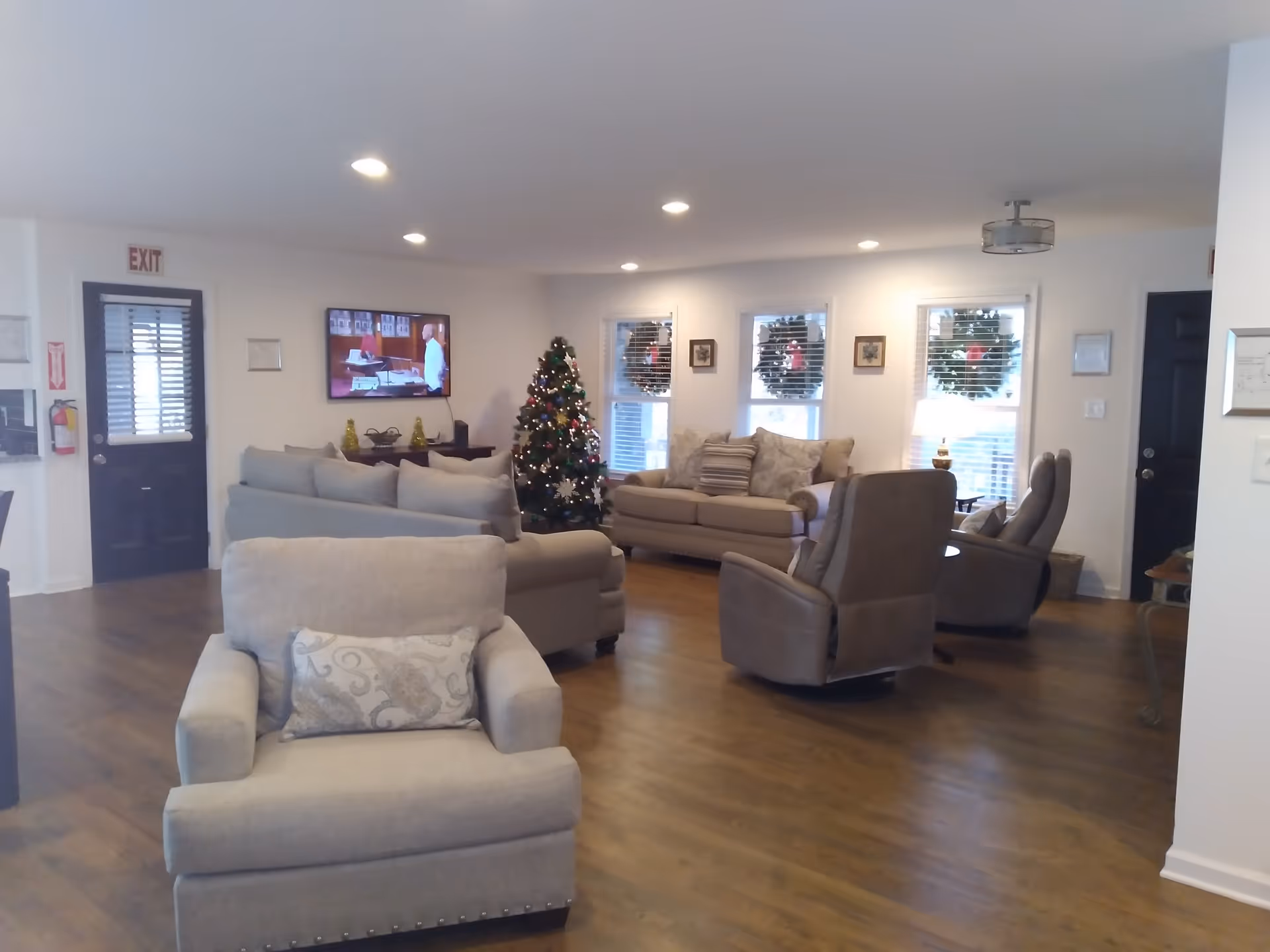 Spacious common living room with sofas, armchairs, a Christmas tree, and a wall-mounted TV.