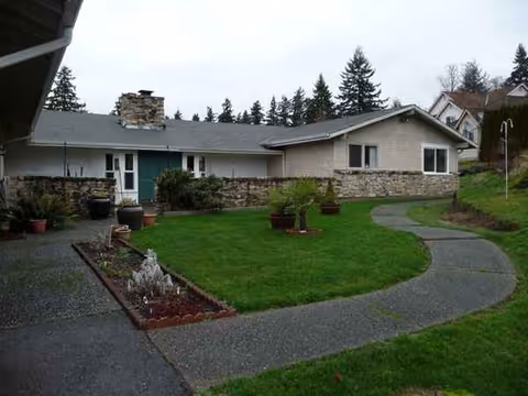 Front exterior of a single-story senior living home with curved walkway and lawn.