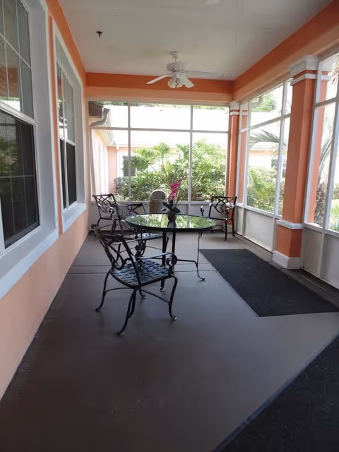Screened-in porch with glass-top bistro tables, wrought-iron chairs, a ceiling fan, and greenery visible through the screens.