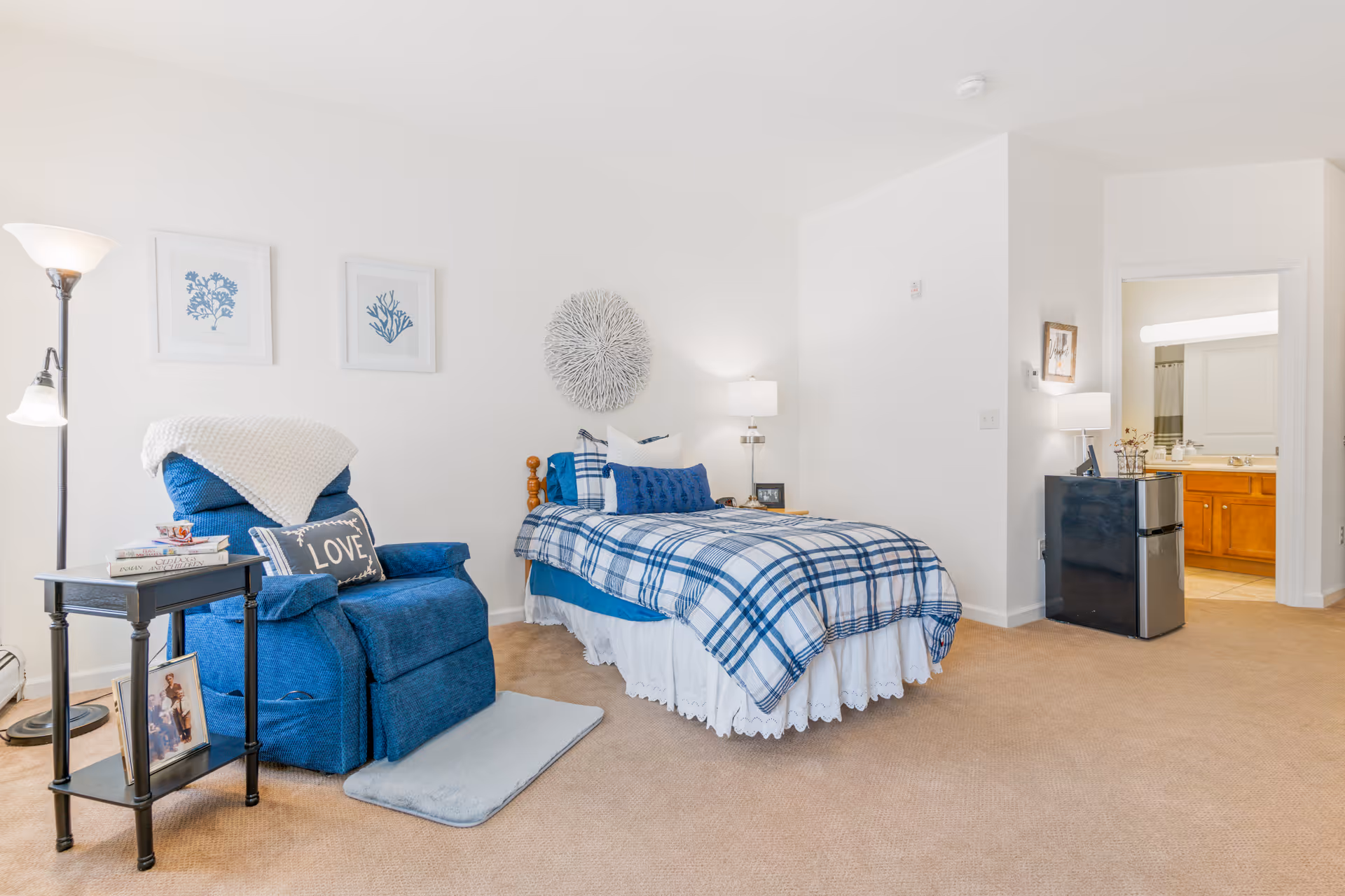 Well-lit bedroom with a single bed in blue plaid bedding, a blue recliner and side table, and an open doorway to a bathroom.