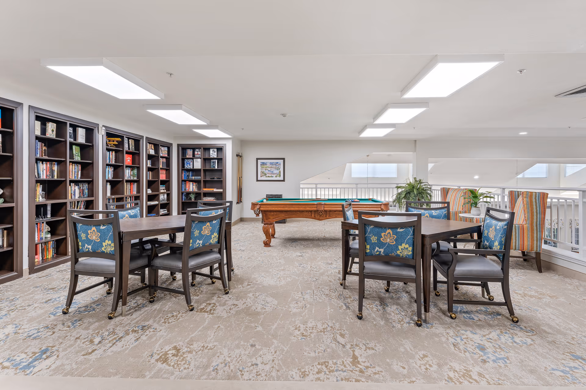 Light-filled communal library and game room with bookshelves, card tables and a pool table.