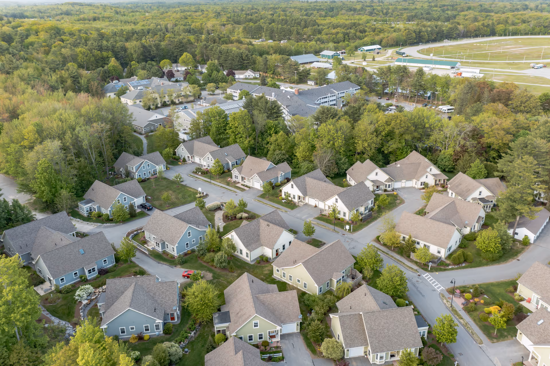 Aerial view of The Highlands senior living facility showing multiple single-story residential buildings surrounded by trees and greenery, with roads and parking areas connecting the buildings.
