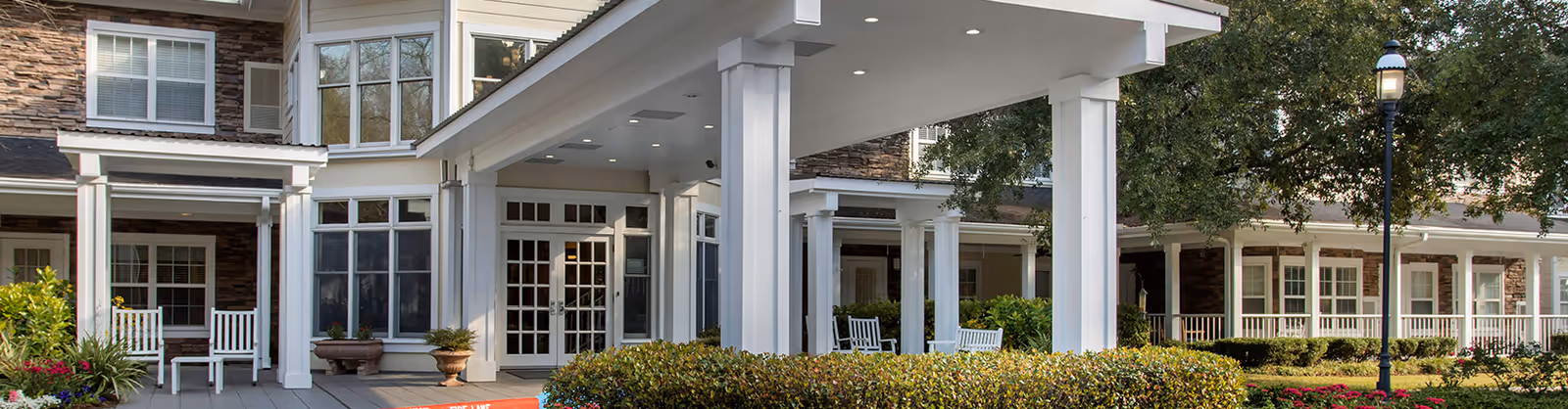 Exterior view of Brookdale Champions showing a covered entrance with white columns and seating.