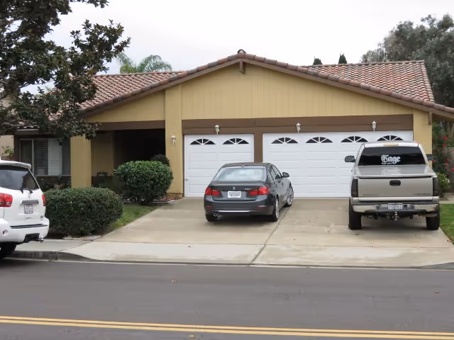 Single-story house with a three-car garage and three vehicles parked in the driveway.