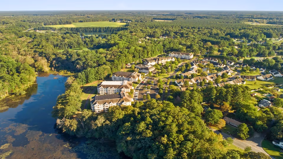 Aerial view of a senior living campus and surrounding neighborhood beside a wooded lake.
